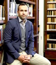 Thomas Faucher Man seated in front of bookshelves