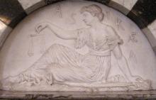marble relief sculpture of seated woman in profile holding a balance scale