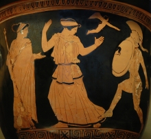 red figures on black background. Helen with raised arms at center, Menelaus cowers behind his shield to the right