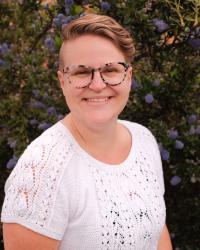 A blonde white woman in glasses smiles and lookes at the camera