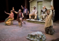 actors sit in front of a small house on stage