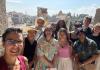 11 individuals stand in front of the ruins of the Roman Forum