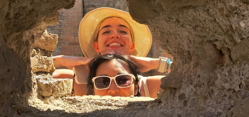 Two smiling students peer through a hole in an ancient wall