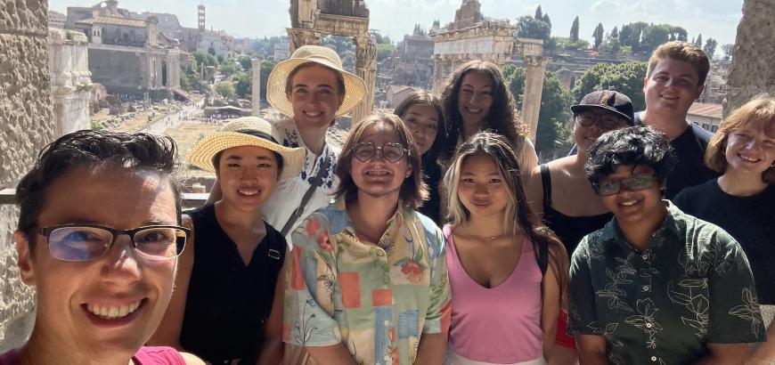 11 individuals stand in front of the ruins of the Roman Forum